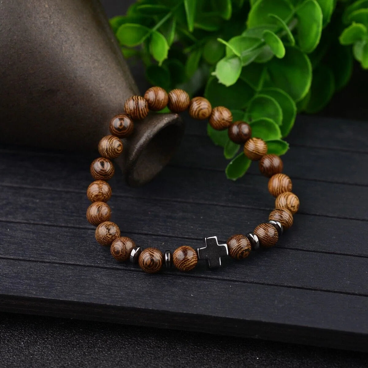 Wooden bead bracelet with cross charm and green plant background