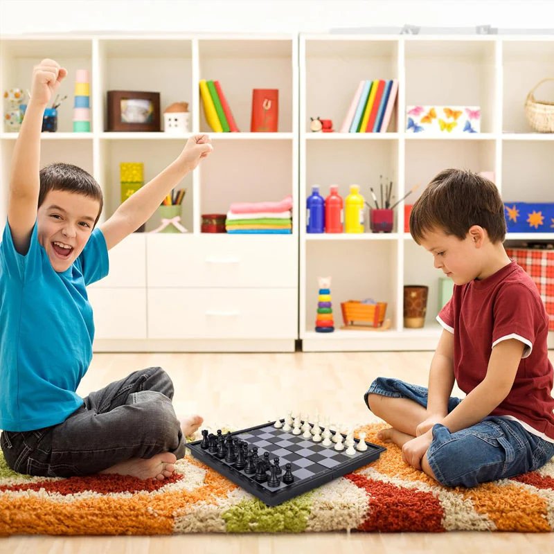Two kids playing chess together on the floor at home