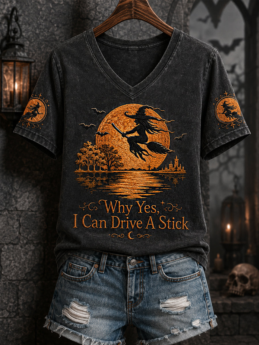 Women's black V-neck Halloween tee with orange witch-on-broom print and 'Why Yes I Can Drive A Stick' text